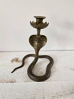 Front view of brass snake candlestick holder showing coiled body and lotus-shaped cup