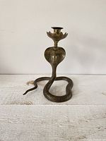 Frontal view showing brass candlestick holder with coiled snake body and detailed cobra hood under candle cup.