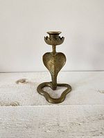 Front view of brass cobra candlestick showing coiled base and spread hood.