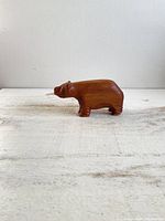 Side view of the vintage wooden bear figurine placed on a light textured surface showing its smooth hand-carved details and natural wood grain.