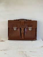 Front view of the brown leather briefcase with embossed crocodile texture, showing the two front metal buckle locks and central buckle strap.