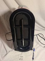 Front view of the air purifier showing black grille and foam filter behind it with pen nearby.