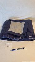 Folded large blue tarp with reinforced corner and grommet visible, pen for size reference