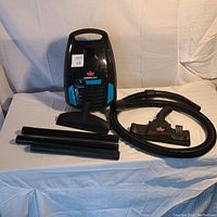 Front view of Bissell PowerForce vacuum with hose, floor brush attachment, and three extension tubes laid out on a white surface.