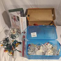 Photo of assorted Christmas decorations including lights, snow globe, Elf on the Shelf box, red brush, and blue container with nativity ornaments.