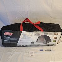 Black carry bag with red straps containing the Coleman 4 Person Skydome Tent. Bag label shows tent picture and setup instructions.