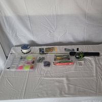 Fishing rod with spinning reel and assorted fishing gear laid out on white cloth