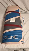 Rolled up GoZone yoga mat in beige, blue, and gray colors secured with red strap alongside a pen for size reference.