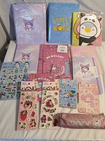 Photo of all stationery folders, notebooks, sticker sheets, and pencil pouch with Hello Kitty, My Melody, Kuromi, Smiley World and animal cartoon designs spread on white surface
