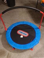 Front top view of children's small trampoline showing blue padding, black jumping mat with Little Tykes logo, red legs, and black handlebar.