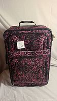 Front view of the suitcase showing pink and black pattern and exterior zippered pockets