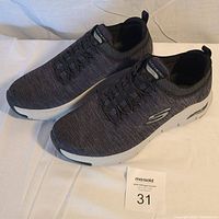 Pair of men's Skechers athletic shoes displayed from top/front angle showing charcoal knit fabric upper, black lace detailing, and white cushioned sole.
