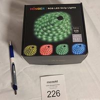 Box of Minger RGB LED strip lights with a green lit strip image and four color options shown on the box, accompanied by a pen for scale and a label with lot number 226.