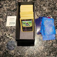 Photo of the Pokémon cards inside a black deck box, card sleeves, dice, and a coin arranged on a countertop.