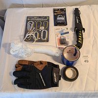 Various tools and hardware supplies including carabiner clips, padlocks, utility knife, rope, tape, and gloves arranged on a white cloth.