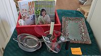 Photo showing red woven basket with cookbooks, nested metal mixing bowls, silicone spoon, clear kitchen timer, and decorative metal tray with red berry accents.