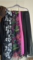 Photo of four floral scarves on a hanger showing different colors and patterns, including black and white flowers, pink and green roses, bright pink solid, and black solid.
