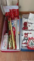 Top view of plastic bin filled with red metallic bows, rolls of Christmas wrapping paper, holiday gift bags, and Christmas cards.