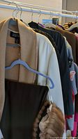 View of assorted coats hanging on a rack showing beige, white, brown coats and a soft gray scarf plus bright red gloves.