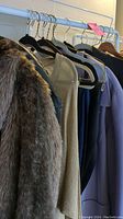 Seven items of women's clothing on hangers including a faux fur coat, knitwear and jackets, shown on a rack.