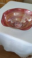 Photo of a large decorative bowl with red and brown gradient colors and wavy rim on a white tablecloth.