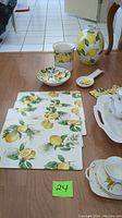 Overall view of lemon-themed tableware including placemats, small bowls, container, and vase
