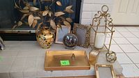Living room decor items displayed on hearth and floor including gold vase with faux leaves, rectangular gold tray, multiple gold frames, gold lantern with candle, round gold clock