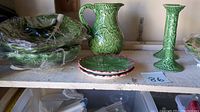 Shelf display of 3 large green cabbage leaf serving trays, a cabbage leaf glazed pitcher, two candlestick holders, and 3 small cabbage leaf plates.