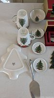 Two mugs, three small dishes, one bowl, tree-shaped platter and serving spoon arranged on a table with visible Christmas Tree design