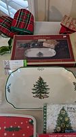 Display of rectangular Spode serving platter with Christmas tree design, oven mitts, gift bags, and napkins