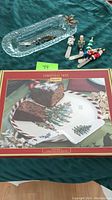 Glass rectangular tray with metal reindeer spreader utensil and three colorful spreader utensils with figurative handles shown on top. Below is a boxed Spode Christmas Tree rectangular serving tray.