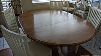 Oval wooden dining table and four white slat-back chairs in dining room setting.