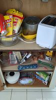 Kitchen items inside cabinet: glass bowls, salad spinner, grater, eggs, plastic wrap, and various kitchen tools.