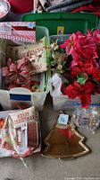 Photo of two bins containing assorted Christmas decorations such as poinsettia flowers, holiday pillows, ribbons, bows, and gift boxes.