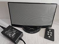 Bose SoundDock speaker with remote control and power adapter in front of a white background.