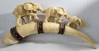 Front view of the carved elephant family on the tusk showing the entire length and detail of the elephants and metal bands.