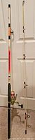 Full view of the Gamefish Neonz 9-foot fishing rod and reel hanging vertically against a white door, showing overall shape, color gradient, and attached reel.