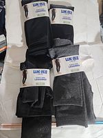 Four pairs of fleece-lined leggings with label showing brand Muk Luks and type fleece-lined leggings in black and dark gray colors, laid flat.