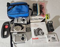 All cameras and accessories in the lot arranged on a surface, including blue carrying case, film, manuals, and batteries.