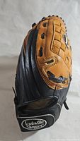 Side view of the Louisville Slugger softball glove showing the black and tan leather with basket weave pattern and logo on wrist strap.