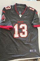 Front view of black Mike Evans Tampa Bay Buccaneers football jersey with red and white number 13 and team logo on sleeve.