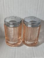 Front view of the pair of pink depression glass salt and pepper shakers with silver metal tops.