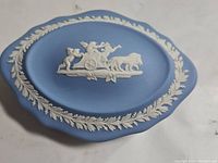 Top view of the blue jasperware trinket box lid showing white classical relief of a chariot and a lion.