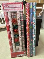 Photo of six rolls of Christmas-themed wrapping paper and six decorative bows arranged together.