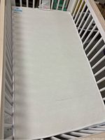 White crib mattress with subtle hexagonal geometric pattern placed inside a white crib frame, showing the entire mattress surface.