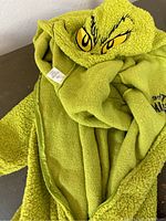 Close-up of the folded green fleece hoodie showing the bright green fuzzy texture and the embroidered Grinch eyes on the hood.