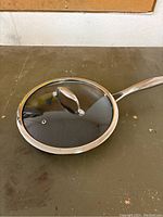 Frying pan with glass lid placed on work surface.