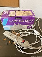 Box of Kirkland Home and Office trash bags and a white extension cord with multiple outlets and power switch on a black surface.