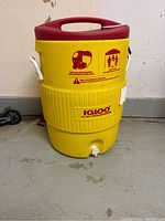 Front view of yellow Igloo water jug with red lid, white handles, spigot, and product instructions on front.