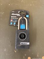 Photo of brand new Master Lock Bluetooth Outdoor Padlock in original packaging showing product front with key features visible on label